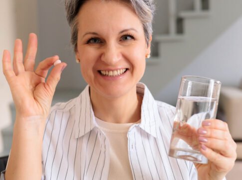A elderly woman pensioner with gray hair holds a pink round contraceptive hormonal pill in her hands Collagen Pills Don't Reach Joints